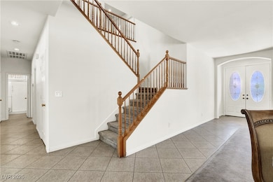 Tiled entrance foyer featuring open wood staircase, white double glass doors, healthy amount of natural light.