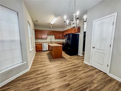 Kitchen featuring a kitchen island, black appliances, hanging light fixtures, a chandelier, and light wood-style floors