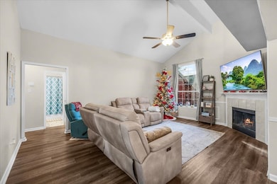 Living room with beam ceiling, a tiled fireplace, high vaulted ceiling, dark wood-style flooring, and a ceiling fan