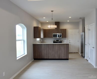 Kitchen with light countertops, hanging light fixtures, modern cabinets, appliances with stainless steel finishes, and light wood-style flooring