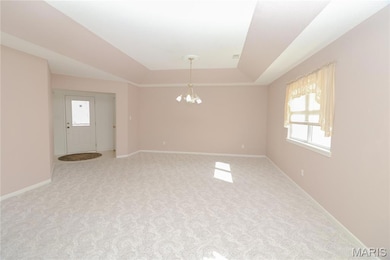 Unfurnished room with a raised ceiling, a chandelier, and light colored carpet