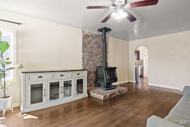 Unfurnished living room featuring a wood stove, arched walkways, dark wood-style floors, and ceiling fan