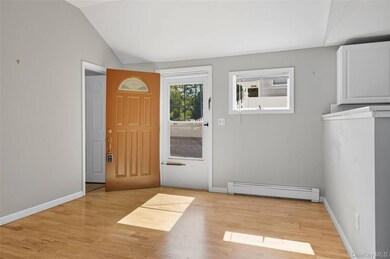 Doorway featuring a baseboard radiator, wood finished floors, and vaulted ceiling