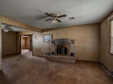 Unfurnished living room featuring a ceiling fan, a fireplace, wood walls, and a textured ceiling