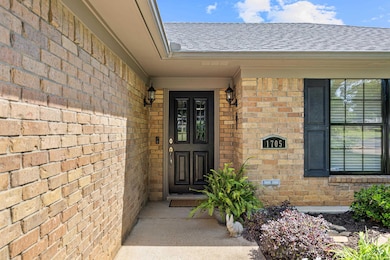 Doorway to property with a shingled roof and brick
