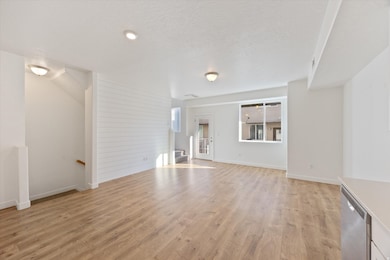 Unfurnished living room with light wood-style flooring, a textured ceiling, stairs, wooden walls, and recessed lighting