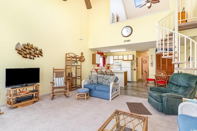 Living room with a ceiling fan, light colored carpet, stairs, and a high ceiling