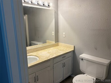 Bathroom with toilet, vanity, a textured wall, and