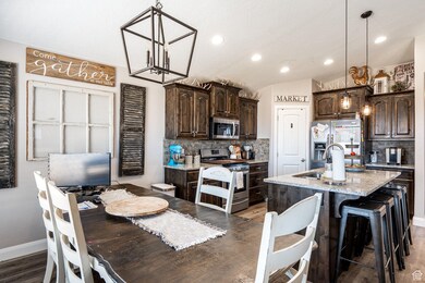Kitchen with dark brown cabinets, appliances with stainless steel finishes, decorative backsplash, light wood-type flooring, and vaulted ceiling