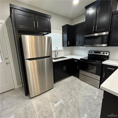 Kitchen featuring dark cabinetry, light marble finish floors, appliances with stainless steel finishes, and recessed lighting