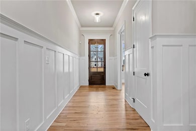 Doorway to outside with a decorative wall, a wainscoted wall, wood finished floors, and ornamental molding