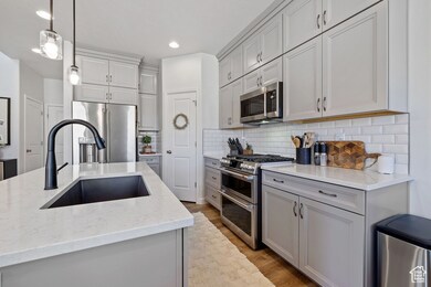 Kitchen featuring backsplash, appliances with stainless steel finishes, light wood-style floors, hanging light fixtures, and a sink