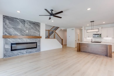 Kitchen featuring white cabinetry, ceiling fan, light hardwood / wood-style floors, decorative light fixtures, and a large fireplace