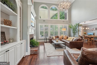 Living area with a chandelier, a fireplace, dark wood-type flooring, a towering ceiling, and healthy amount of natural light