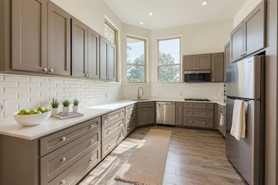 Kitchen with appliances with stainless steel finishes, gray cabinets, light stone countertops, light wood finished floors, and backsplash