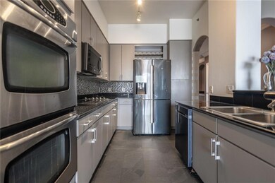 Kitchen with stainless steel appliances, arched walkways, dark countertops, gray cabinetry, and tasteful backsplash