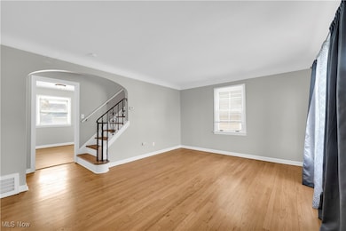 Unfurnished living room with arched walkways, light wood-type flooring, and stairs