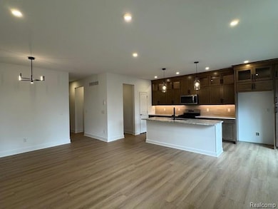 Kitchen featuring decorative light fixtures, dark brown cabinets, a center island with sink, open floor plan, and light wood-type flooring