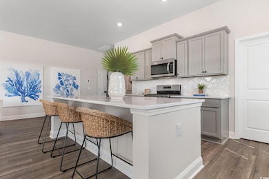 Kitchen with gray cabinets, stainless steel appliances, a kitchen island, dark wood-type flooring, and recessed lighting