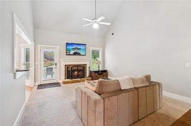 Living room with light colored carpet, a ceiling fan, plenty of natural light, a stone fireplace, and high vaulted ceiling
