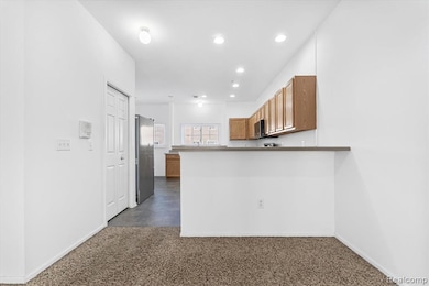 Kitchen with brown cabinets, freestanding refrigerator, recessed lighting, dark carpet, and a peninsula