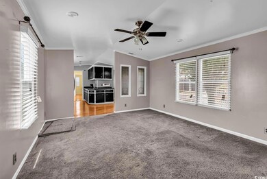 Carpeted empty room featuring ceiling fan, baseboards, vaulted ceiling, and crown molding