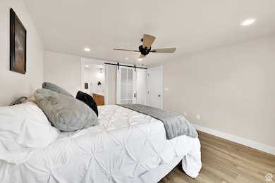 Bedroom featuring a barn door, wood finished floors, ceiling fan, recessed lighting, and ensuite bath