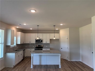 Kitchen with decorative backsplash, hanging light fixtures, stainless steel appliances, white cabinetry, and recessed lighting
