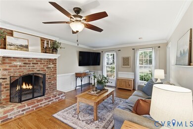 Living area with crown molding, wood finished floors, a brick fireplace, a wainscoted wall, and ceiling fan