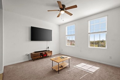 Carpeted living area featuring a ceiling fan and baseboards