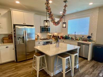 Kitchen with white cabinets, stainless steel appliances, a kitchen breakfast bar, a kitchen island, and recessed lighting