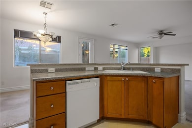 Kitchen featuring brown cabinetry, white dishwasher, decorative light fixtures, an island with sink, and light carpet