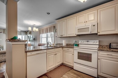 Kitchen with light wood-type flooring, white appliances, a chandelier, kitchen peninsula, and cream cabinets