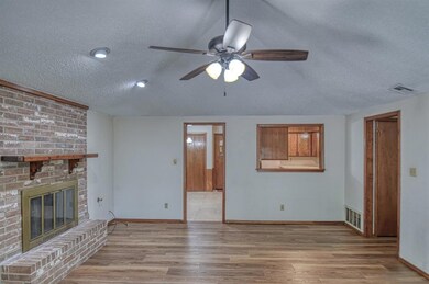 Unfurnished living room featuring light hardwood / wood-style flooring, a brick fireplace, ceiling fan, and a textured ceiling