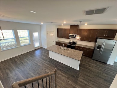 Kitchen featuring dark brown cabinets, appliances with stainless steel finishes, decorative light fixtures, a kitchen island with sink, and recessed lighting