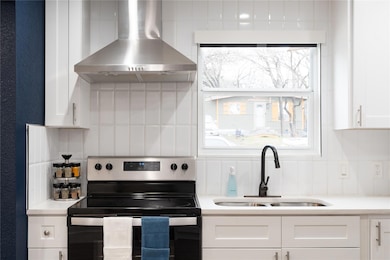Kitchen featuring backsplash, stainless steel range with electric cooktop, wall chimney range hood, white cabinets, and light countertops