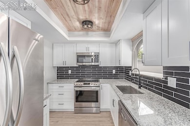 Kitchen featuring appliances with stainless steel finishes, a raised ceiling, a sink, wood ceiling, and white cabinetry