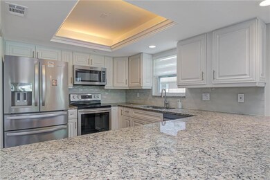 Kitchen with sink, white cabinetry, light stone counters, appliances with stainless steel finishes, and a tray ceiling
