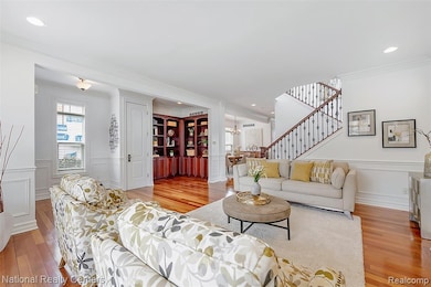 Living area featuring wainscoting, light wood-type flooring, crown molding, a chandelier, and stairs