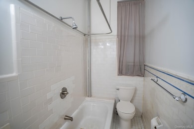 Bathroom with tiled shower / bath combo, toilet, and tile walls