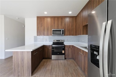 Kitchen featuring stainless steel appliances, backsplash, modern cabinets, light stone countertops, and a peninsula