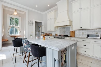 Kitchen featuring premium range hood, backsplash, crown molding, light stone countertops, and white cabinets