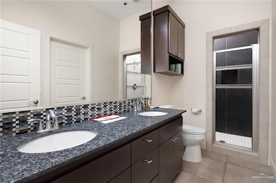 Bathroom with tasteful backsplash, tile patterned flooring, toilet, a shower with door, and vanity