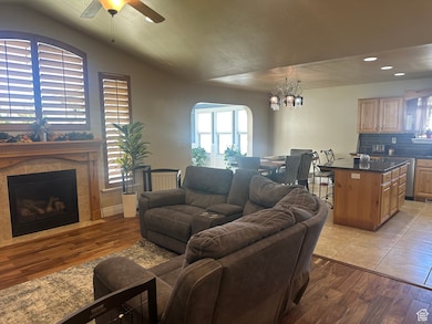 Living room with ceiling fan, arched walkways, a tiled fireplace, light wood-style flooring, and vaulted ceiling