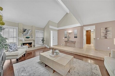 Entry Door with Glass Block Sidelight Opens to Travertine Raised Foyer and Large Formal Living Room with Soaring Ceiling, Wood Laminate Flooring, Plantation Shutters, and Fireplace with Raised Travertine Hearth