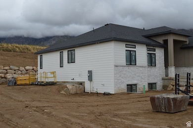Rear view of property featuring stone siding, roof with shingles, and a patio area