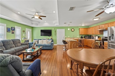 Living area featuring a ceiling fan, light wood-type flooring, recessed lighting, and a tray ceiling