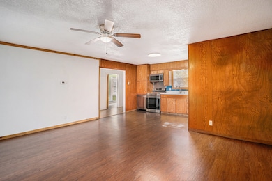 Kitchen with light countertops, appliances with stainless steel finishes, brown cabinets, dark wood-style floors, and a textured ceiling