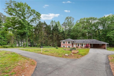 Split level home with a front lawn, an attached carport, a forest view, and aphalt driveway