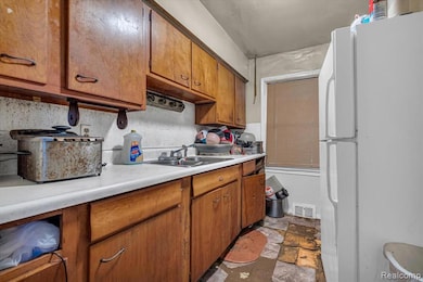 Kitchen with freestanding refrigerator, light countertops, brown cabinets, and dark stone finish flooring